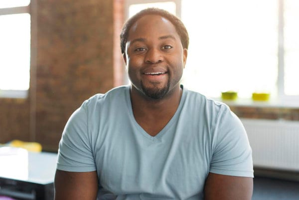 A black man displaying mental health in an office with a smile on his face.