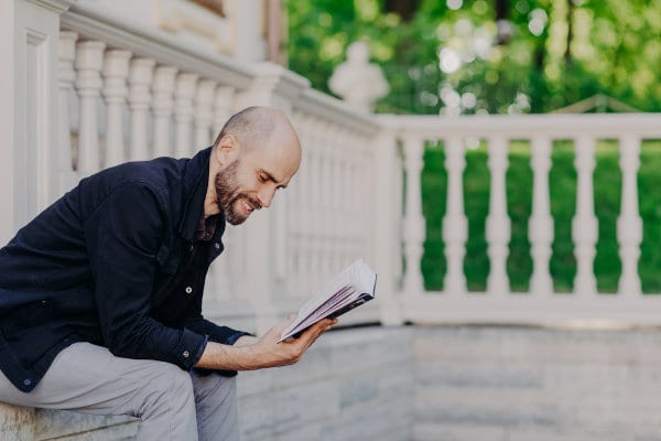 A man promoting mental health by sitting on the steps reading a book.