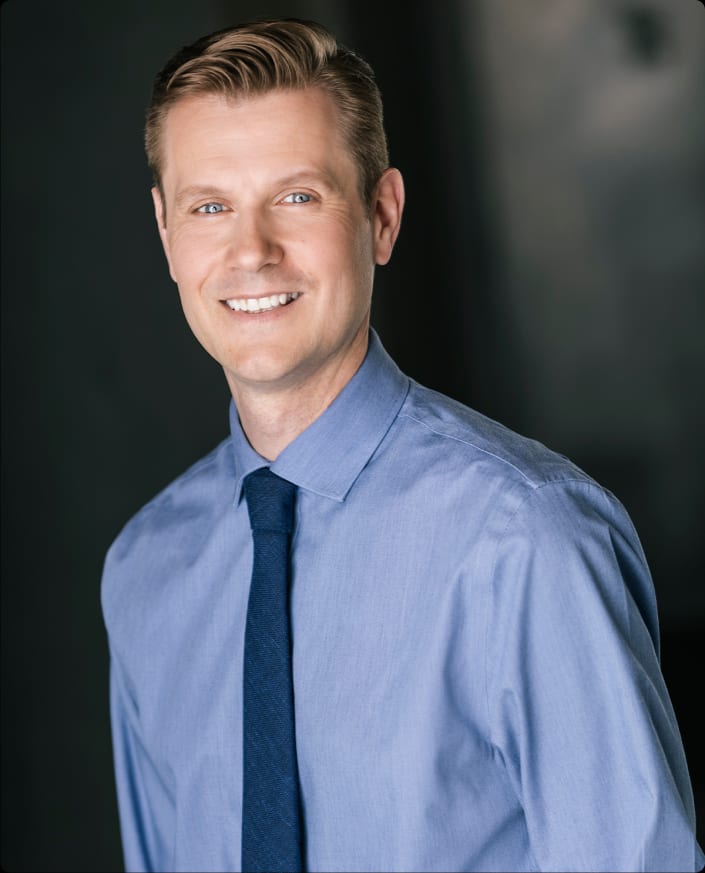 Jordan Penner, a smiling man in a blue shirt and tie.