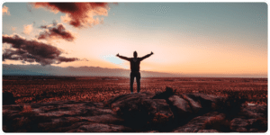 A man embracing mental health while standing on top of a rock with his arms outstretched.